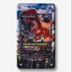 May include: A rectangular acrylic display case for a trading card, featuring a printed background of a Charizard V Pokémon card. The case has four silver corner screws and displays the text "Cards not included" in yellow on the front surface.