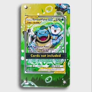 May include: A rectangular acrylic display case featuring a green background with white bubble graphics. The case holds a Blastoise & Piplup GX trading card with 270 HP. A black horizontal banner across the center displays the text Cards not included.