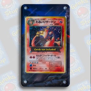 Può includere: Una carta da gioco giapponese Pokemon con un Charizard rosso e arancione su sfondo nero. La carta è in una custodia protettiva di plastica con una cornice nera. Il testo della carta recita "わるいリザードン" e "LV.38 HP80".