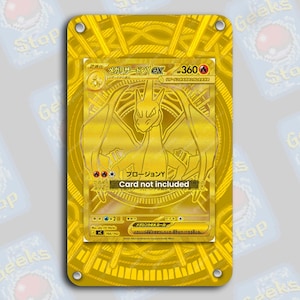 May include: A gold-colored display case with a gold Charizard EX trading card. The card is in Japanese and features a dragon illustration. The text "Card not included" is visible. The case has rounded corners and four holes.