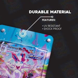 May include: A clear plastic card protector with a blue and pink design, holding a Sylveon VMAX Pok&eacute;mon card. The protector is labeled "Durable Material" and features UV resistance and shock proofing.