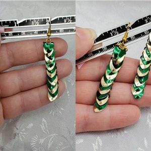 Op de afbeelding: Een paar groene en gouden oorhangers met een schubbenachtig ontwerp. De oorhangers zijn ongeveer 5 cm lang.