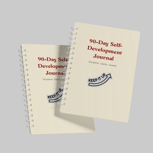 Puede incluir: Dos diarios en espiral de color crema con el texto "90-Day Self-Development Journal" en rojo. Los diarios tienen el texto "Discipline - Clarity - Growth" y un gráfico de flecha "KEEP IT UP". Los diarios están sobre un fondo gris claro.
