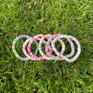 Könnte beinhalten: Ein Set aus sechs bunten Armbändern aus kleinen, runden Perlen. Die Armbänder sind rosa, weiß, grün und gelb.