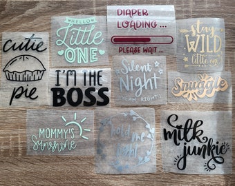 May include: Nine iron-on vinyl designs for clothing or other crafts. The designs include phrases like "Cutie Pie", "Little One", "I'm the Boss", "Mommy's Sunshine", "Hold Me Tight", "Milk Junkie", "Diaper Loading", "Silent Night", and "Stay Wild".