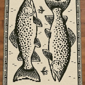May include: A rectangular crochet blanket featuring a cream-colored background with two large, dark green fish oriented in opposite directions. The design includes small green fishing fly motifs and a geometric border pattern along the left and right edges.