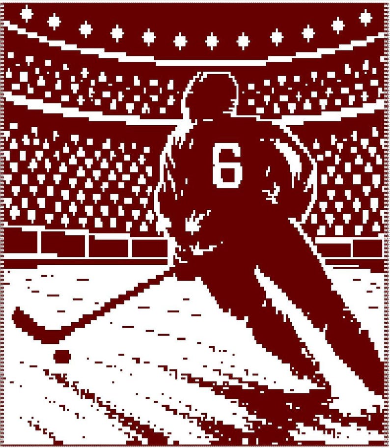 May include: A maroon and white woven blanket featuring a pixelated graphic of a hockey player wearing a jersey with the number 6 on the back. The player is positioned on an ice rink with a hockey stick and puck, set against a stadium crowd.