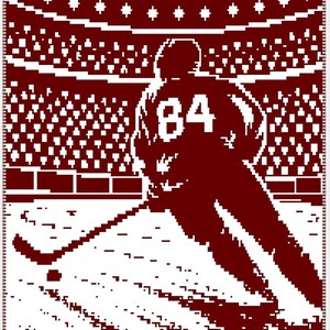 May include: A maroon and white woven blanket featuring a pixelated graphic of a hockey player wearing a jersey with the number 84. The player is shown on the ice with a hockey stick and puck, set against a stadium background with a crowd.