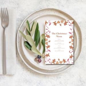 Op de afbeelding: Een witte, afdrukbare kerstmenukaart met een rand van gingerbread man, snoepstokken en harten. De tekst "The Christmas Menu" staat in bruine tekst bovenaan de kaart.