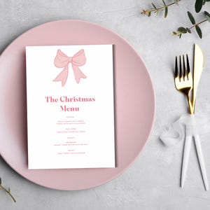 Op de afbeelding: Een roze en wit printbaar kerstmenu met een roze strik bovenaan. Het menu bevat de tekst "The Christmas Menu" en somt de voorgerechten, hoofdgerechten, desserts en dranken op.