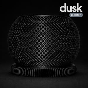 Puede incluir: Una maceta esférica negra con un exterior con diseño de diamantes, apoyada sobre una base circular con líneas verticales. La palabra "dusk" está encima de la palabra "planter" en un rectángulo blanco.
