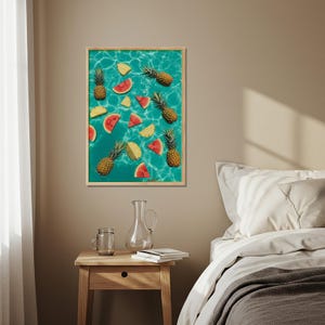 Op de afbeelding: Een ingelijste print met ananassen en watermeloenpartjes die op een turquoise waterachtergrond drijven. De vruchten zijn in een willekeurig patroon gerangschikt, wat een verfrissende en zomerse uitstraling creëert. De lijst is licht van kleur.