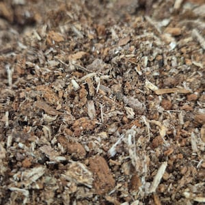 Könnte beinhalten: Nahaufnahme eines Haufens brauner und beiger Holzspäne und Rinde. Die Textur ist rau und uneben, mit Holzstücken unterschiedlicher Größe und Form. Das Bild zeigt die natürlichen Farben und Details des organischen Materials.
