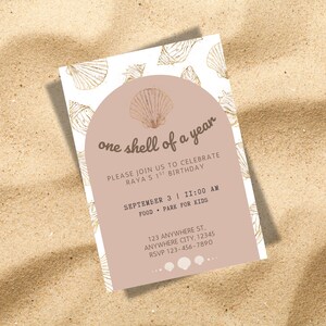 Pode incluir: Um convite de aniversário com tema de concha. O convite apresenta o texto "one shell of a year" em uma fonte elegante, juntamente com os detalhes do evento. O design inclui ilustrações de conchas e é colocado em um fundo arenoso.
