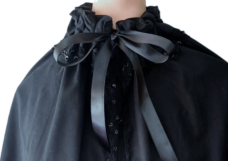 May include: A black velvet cape with a ruffled collar and a black satin ribbon tied at the neck. The cape is decorated with black sequins.