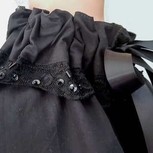 May include: A black ruffled collar with a black lace trim and black ribbon tied at the back.