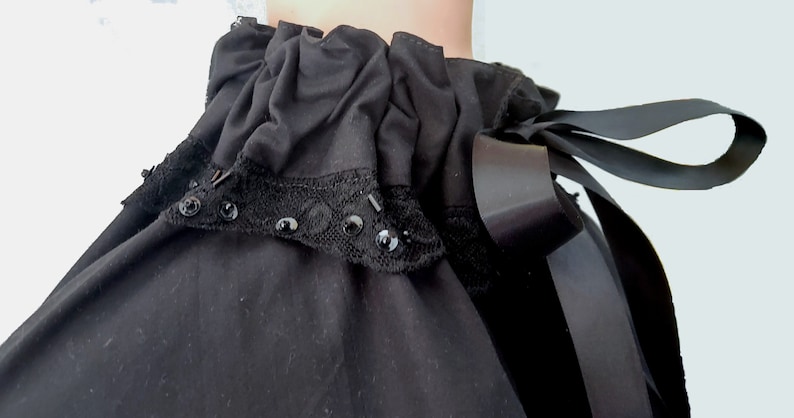 May include: A black ruffled collar with a black lace trim and black ribbon tied at the back.