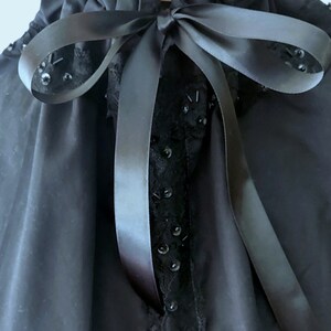 May include: A black blouse with a ruffled collar and a black satin ribbon tied in a bow. The blouse has black lace trim and black sequins.