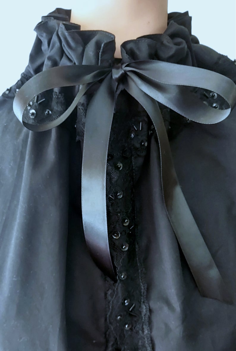 May include: A black blouse with a ruffled collar and a black satin ribbon tied in a bow. The blouse has black lace trim and black sequins.