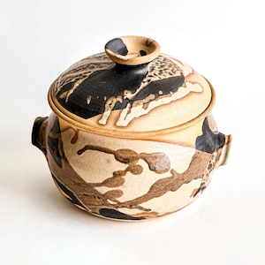 May include: A ceramic casserole dish with a lid. The dish is decorated with a brown and black abstract pattern on a beige background.