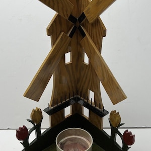 May include: Wooden corner shelf shaped like a windmill with a small pot in the center. The windmill has four blades and is painted brown. The shelf is painted green and has two red and yellow tulips on each side.