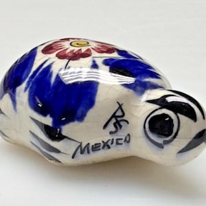 May include: A ceramic turtle figurine with a white base, blue and red floral design, and black accents. The word "MEXICO" is written on the side. The turtle has a detailed face with large black eyes.