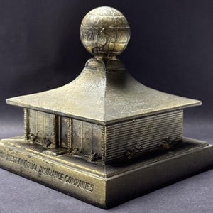 May include: A bronze-colored miniature building with a globe on top. The building has a pagoda-like roof and the text "MID-WEST NATIONAL INSURANCE COMPANIES" on the base. The globe has the word "NATION" on it.
