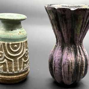 May include: Two ceramic vases. The vase on the left is a small, brown vase with white and brown patterns and a light green top. The vase on the right is a larger, purple vase with a textured surface.