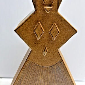 May include: A brown ceramic sculpture with a textured surface featuring a wide top, a central diamond-shaped section, and a flared base. The piece is decorated with incised geometric patterns, including diamonds and triangles, and vertical lines.
