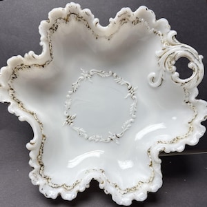 May include: White, scalloped-edge serving bowl with a floral design in the center and gold trim. The bowl has a star-like shape with ornate handles and a glossy finish. A decorative piece for serving.