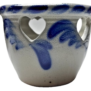 Puede incluir: Pequeño cuenco de cerámica blanquecina con detalles azules y cortes en forma de corazón. El borde presenta una serie de formas azules de lágrima. El cuenco tiene una superficie texturizada y una forma redondeada, ideal para plantas pequeñas.