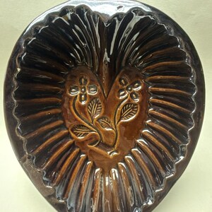 May include: A brown ceramic heart-shaped baking dish with a handle. The dish has a raised design of leaves and flowers.