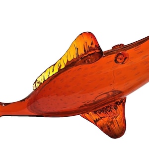 May include: A decorative glass sculpture of a fish in shades of orange and yellow. The fish has a long, pointed snout, a dorsal fin, and a forked tail. The glass is translucent, allowing light to pass through, and is likely a decorative item.