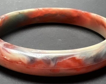 May include: A red, white, and blue marbled bangle bracelet. The bracelet is made of a smooth, polished material.