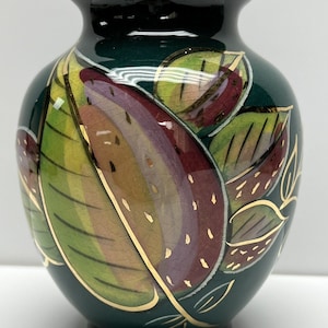 May include: A dark green ceramic vase with a glossy finish. The vase is decorated with stylized leaves in shades of green, red, and yellow, outlined with gold accents. The vase has a rounded body and a narrow neck.