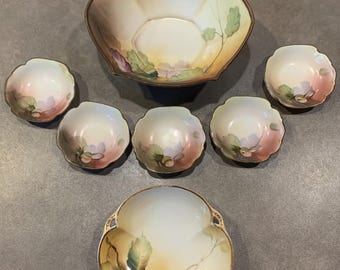 May include: A set of seven vintage porcelain bowls with a floral design. The bowls are in shades of white, yellow, pink, and green. The largest bowl has a scalloped edge and the smaller bowls have a rounded shape. The bowls are all decorated with a floral design featuring leaves, flowers, and acorns.