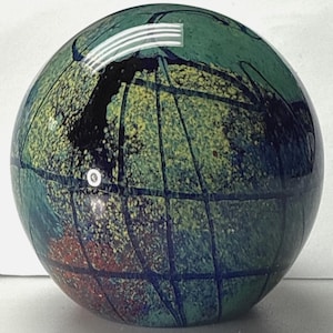 May include: A decorative glass sphere with a globe design. The sphere features a mix of green, blue, yellow, and red colours. Dark blue lines create a grid pattern across the surface, with a black area near the top.