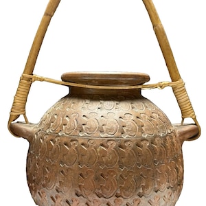May include: A brown, round ceramic pot with a bamboo handle. The pot is decorated with a repeating pattern of stylized figures. The handle is attached with woven twine. The pot has a lid and two small handles on the sides.
