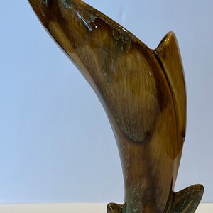 May include: A brown ceramic vase with a unique, curved design. The vase has a mottled brown and green glaze with a glossy finish.