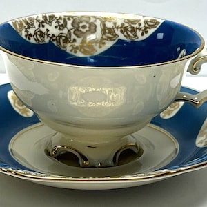 May include: A white teacup and saucer set with a blue and gold floral design. The cup has a footed base and a delicate handle. The saucer has a scalloped edge.