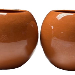 May include: Two spherical ceramic planters with a smooth, glossy, burnt orange finish. Each planter features a wide, circular opening at the top and a rounded, bulbous body, presenting a uniform, solid color appearance without any additional patterns.