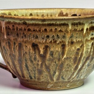 May include: A handmade ceramic mixing bowl with a handle and a pouring spout. The bowl features a textured surface with brown, tan, and cream-colored glazes. The pottery bowl is suitable for kitchen use.