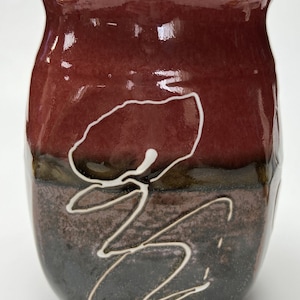 May include: A ceramic vase with a dark red, brown, and black glaze. The vase has a white floral design painted on the front.