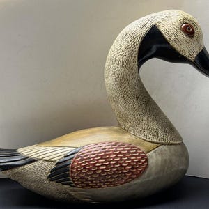 May include: A hand-carved wooden goose figurine with a white, brown, and red painted finish. The goose has a long neck and a detailed beak.