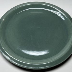 May include: A plain, round, green ceramic dinner plate.