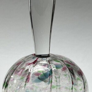 May include: A clear glass bottle stopper with a long, thin handle. The bottle stopper has a round, textured base with pink, green, and blue flecks.