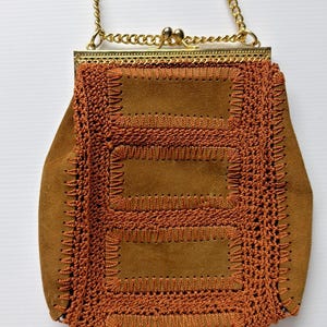 May include: A vintage brown suede handbag with a gold chain strap and clasp. The bag features intricate crochet and stitched detailing in a darker brown color, creating a textured, geometric pattern. The bag is a small, shoulder-style purse.