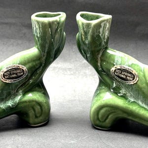 May include: A pair of green ceramic candle holders shaped like a shoe. Each holder has a label that reads "Hot Springs National Park".