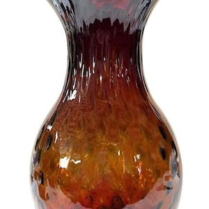 May include: A glass vase with a wide mouth and a round body. The vase is made of clear glass with a mottled, amber and burgundy color scheme. The vase has a textured surface with small bubbles throughout.