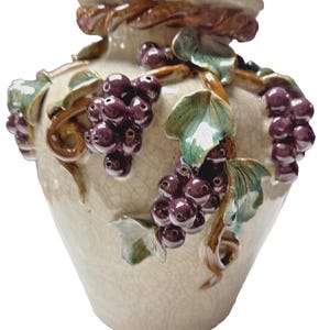 May include: A ceramic vase with a cream-colored crackle glaze finish, featuring three-dimensional sculpted purple grape clusters and green leaves wrapped around the exterior, topped with a brown twisted rope-style decorative rim.